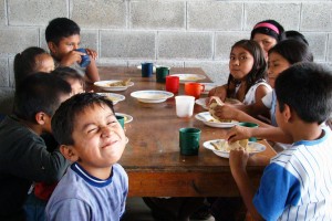 Niños y voluntarios comparten comida.